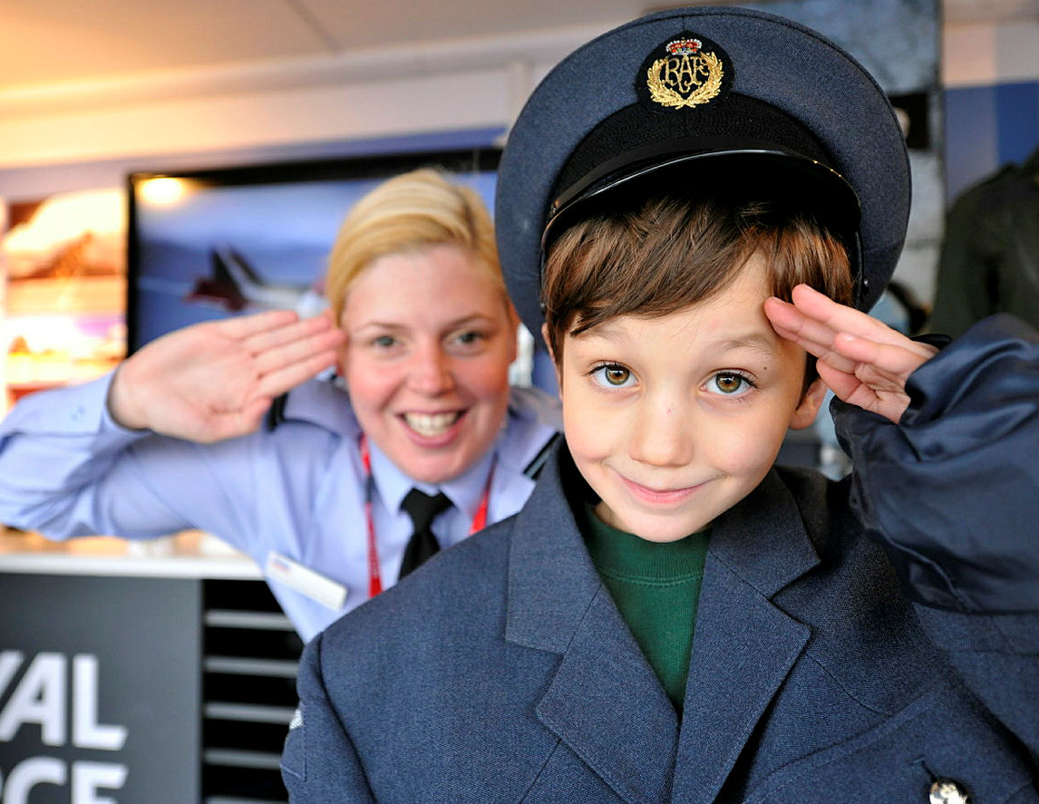 Image shows RAF aviator saluting with child dressed in oversized RAF uniform.